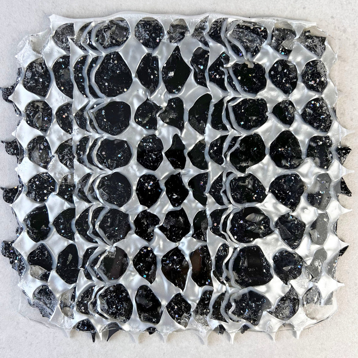 A melt pressed recycled acrylic sheet comprising of black and pearlescent acrylic scraps pressed within. Moon phase shapes are present.