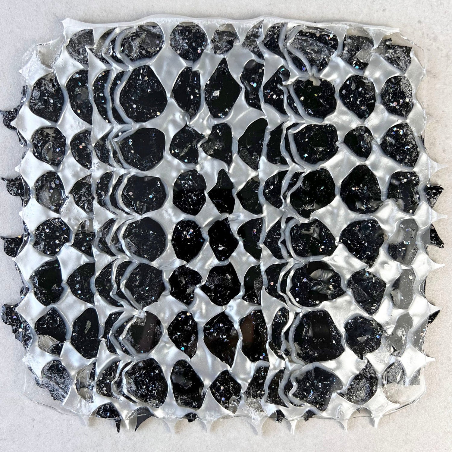 A melt pressed recycled acrylic sheet comprising of black and pearlescent acrylic scraps pressed within. Moon phase shapes are present.