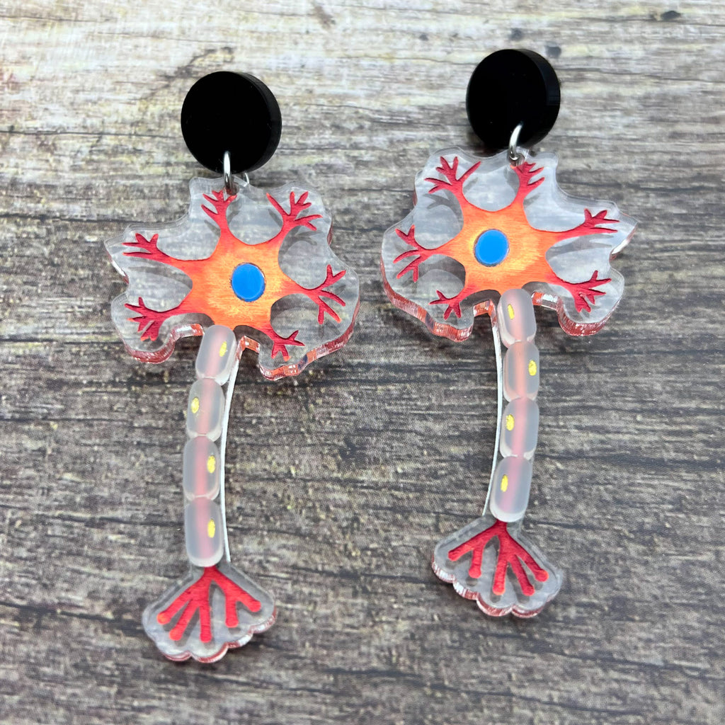Close up view of laser cut acrylic neuron earrings being modelled. Earrings are cut from transparent acrylic, with the neuron design engraved and handpainted. The neurons hang from black earring toppers. 