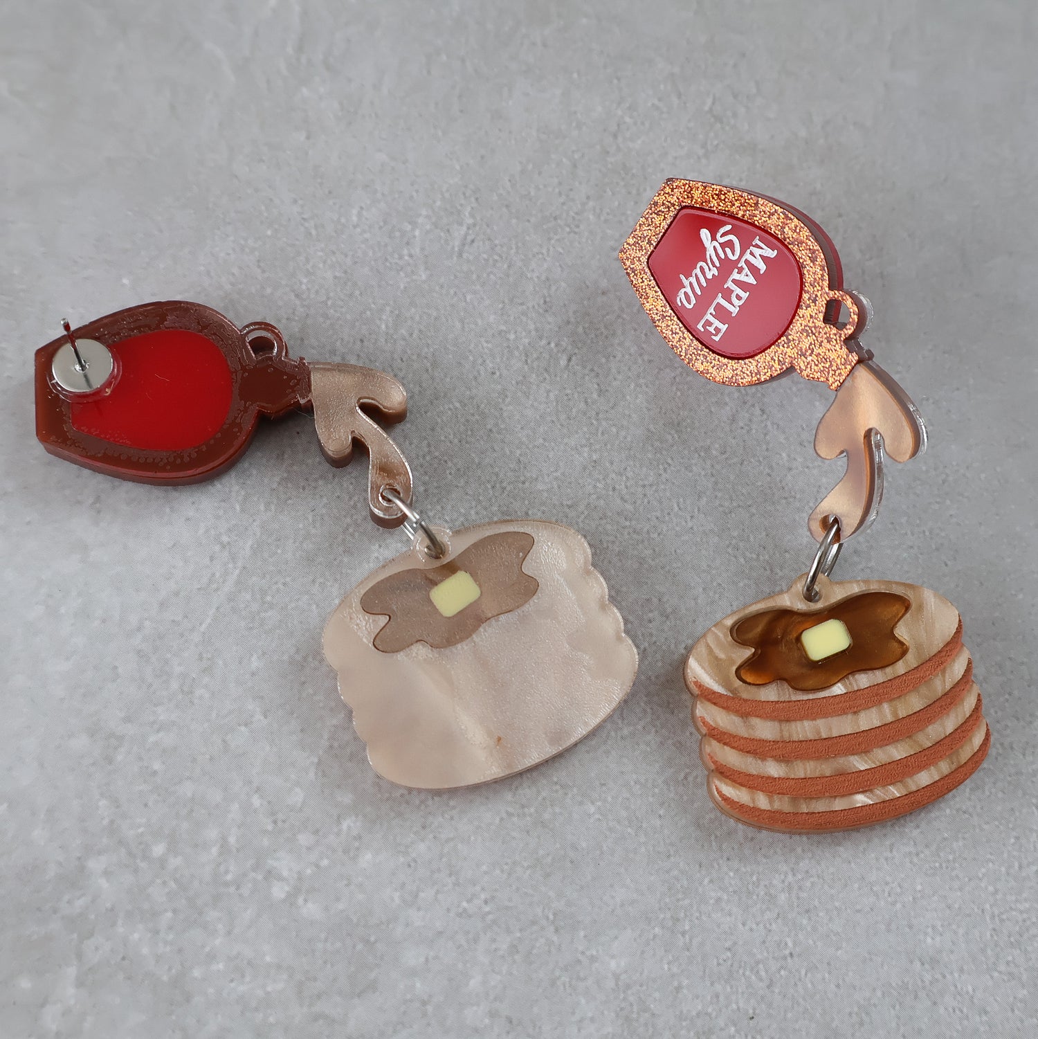 Pair of earrings shaped like pancakes with syrup on a gray background