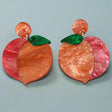 A pair of peach earrings with orange and red and green marbled acrylics on a gray background
