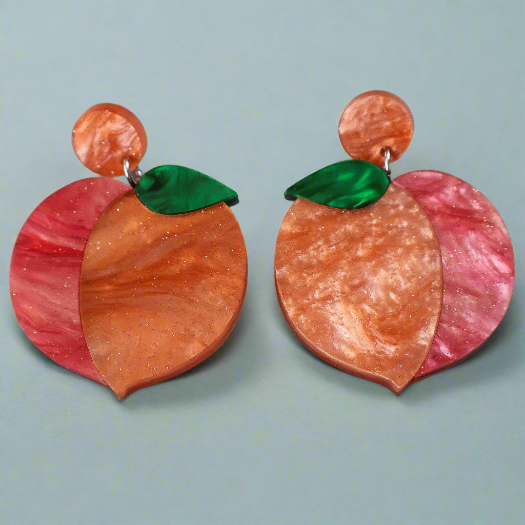 A pair of peach earrings with orange and red and green marbled acrylics on a gray background