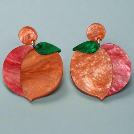 A pair of peach earrings with orange and red and green marbled acrylics on a gray background