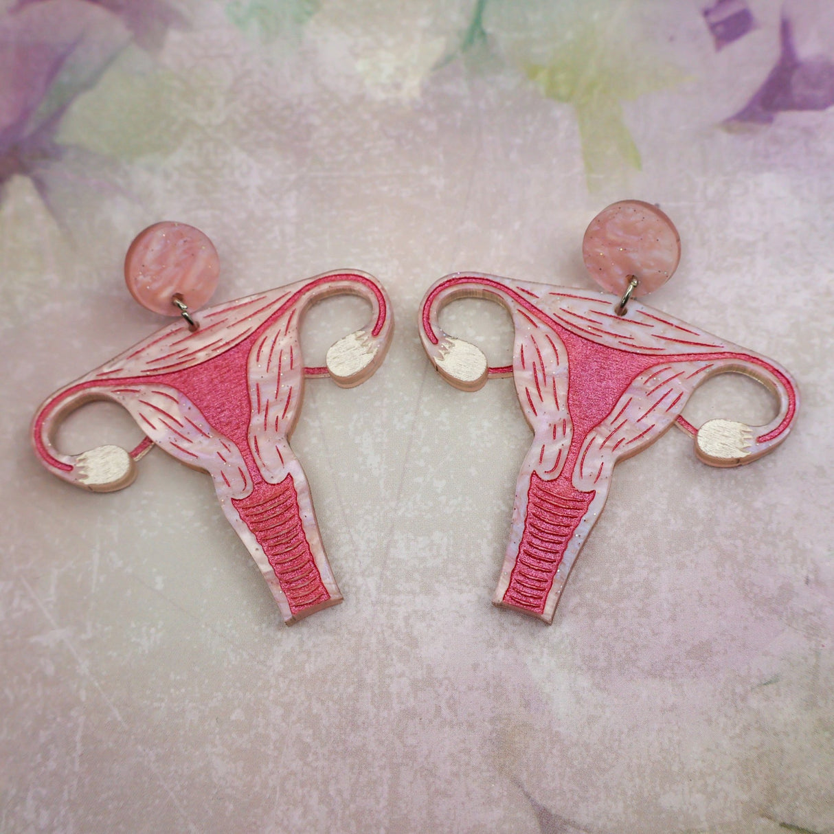Acrylic dangle Earrings shaped like a uterine cervix against a floral background.