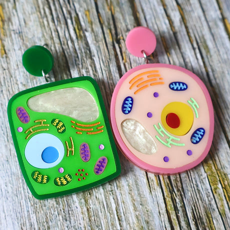 Two colourful asymmetrical acrylic earrings resembling plant and animal cell models on a wooden surface.
