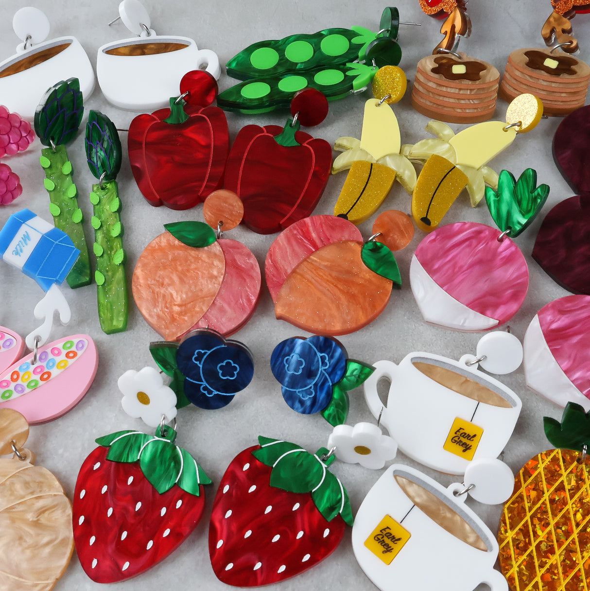 Colorful earrings shaped like fruits, vegetables, and tea bags on a light gray background