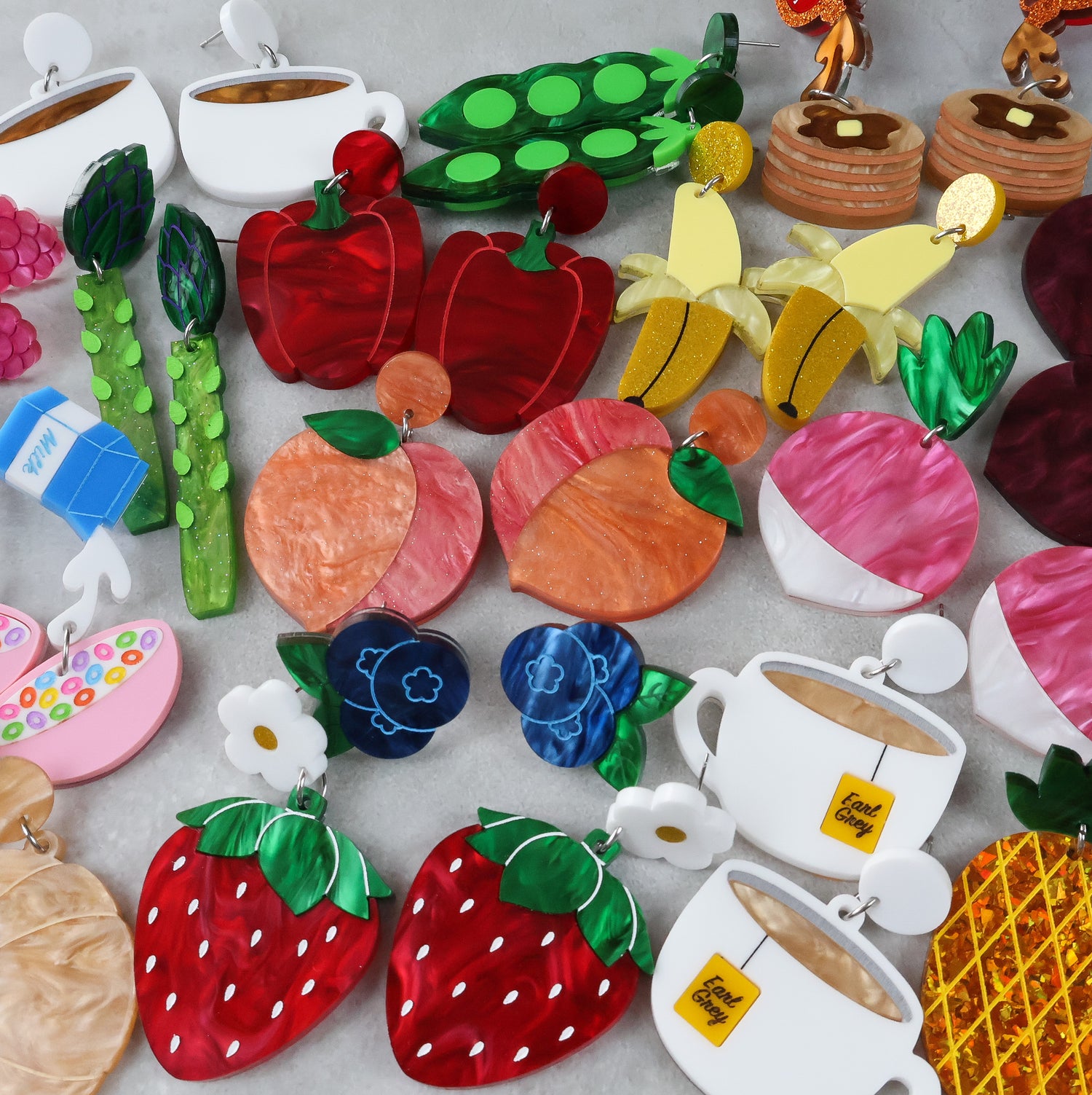 Colorful earrings shaped like fruits, vegetables, and tea bags on a light gray background