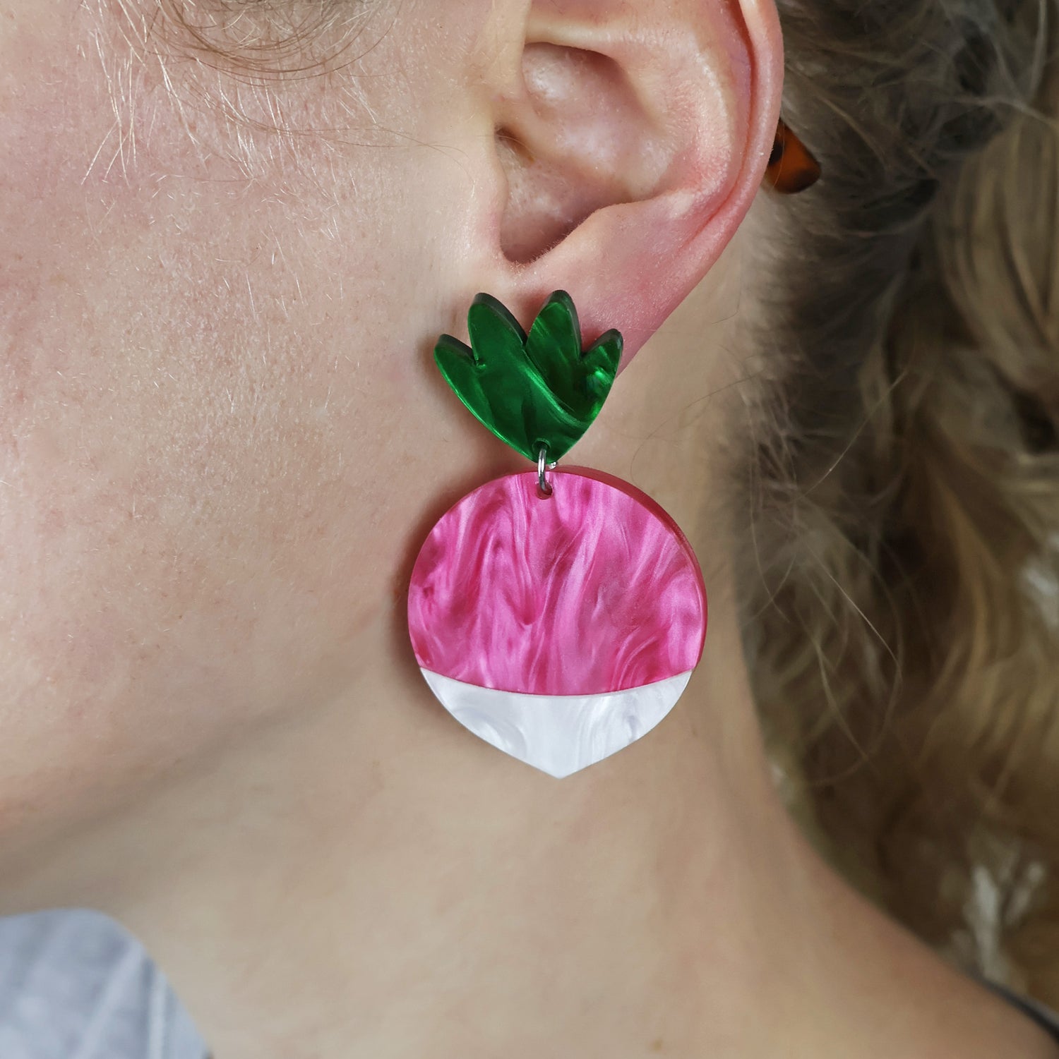 Close-up of a person wearing a radish earring with a pink and white body and green topper.