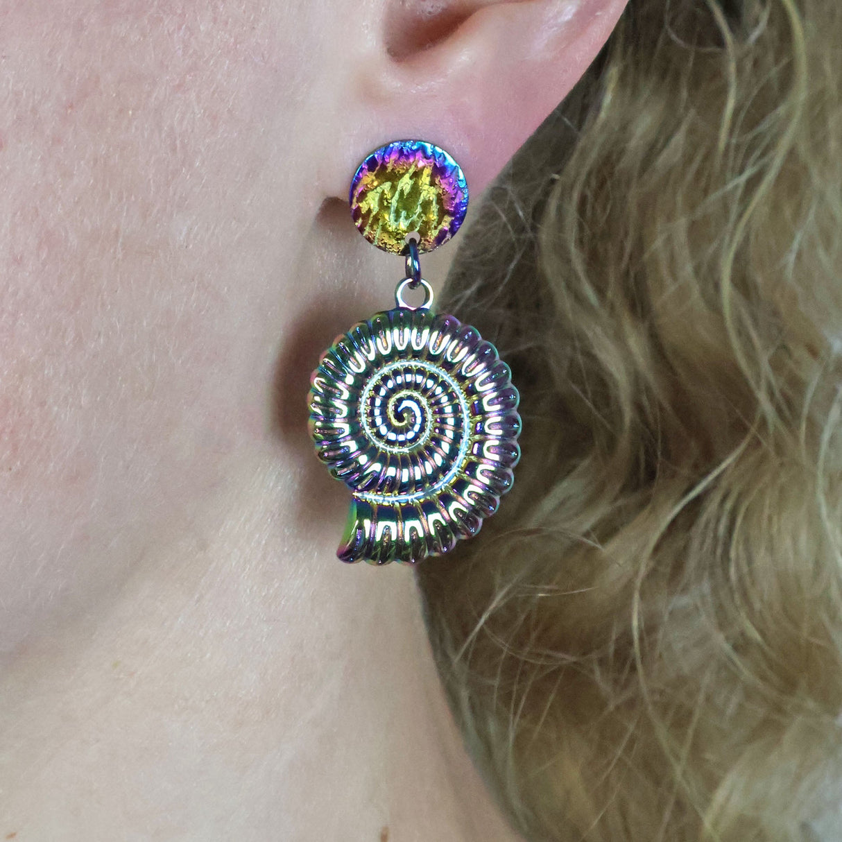 rainbow stainless steel spiral shell earrings worn on an ear with blonde hair.