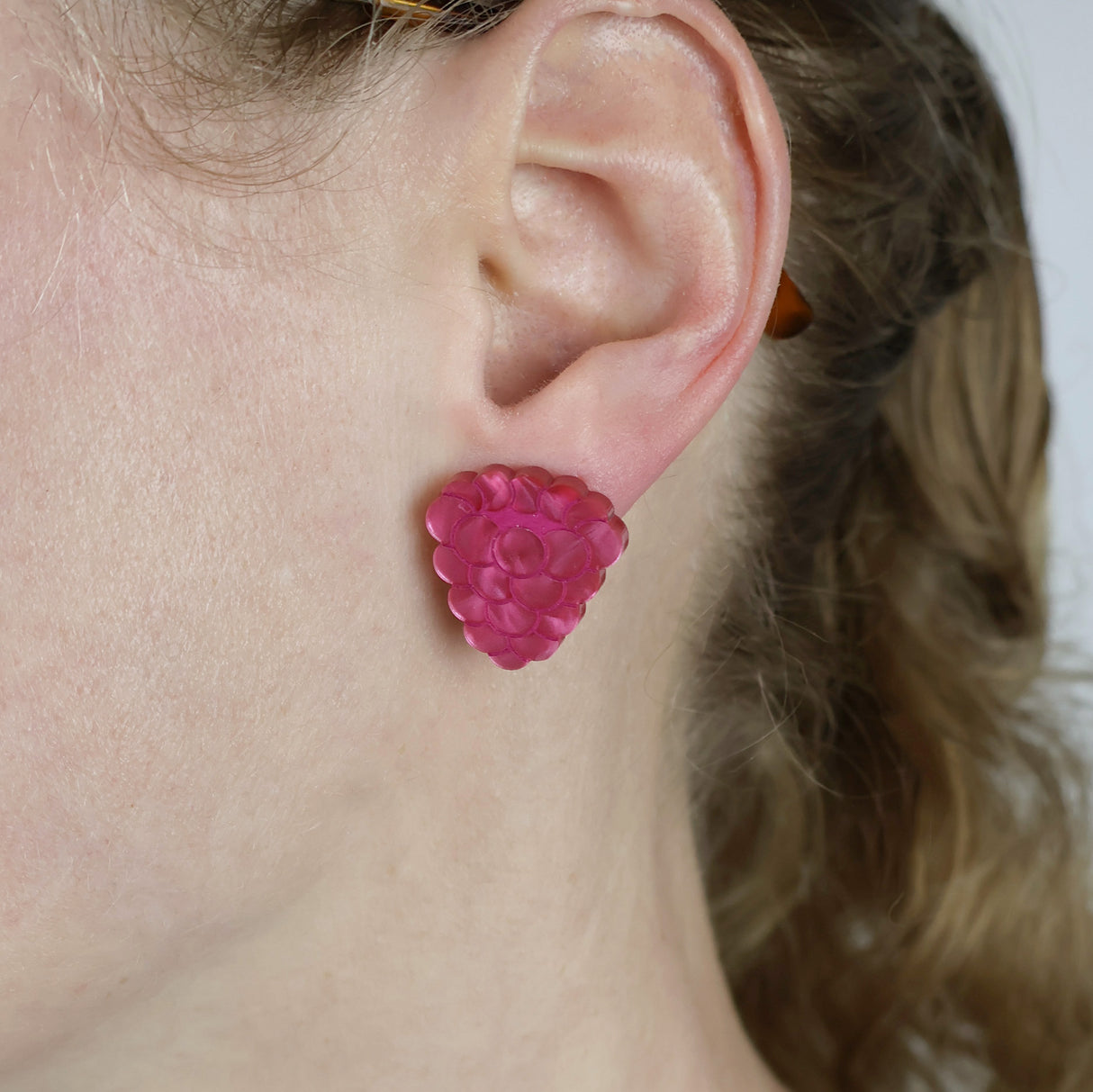 Close-up of an ear wearing a pink raspberry-shaped earring.