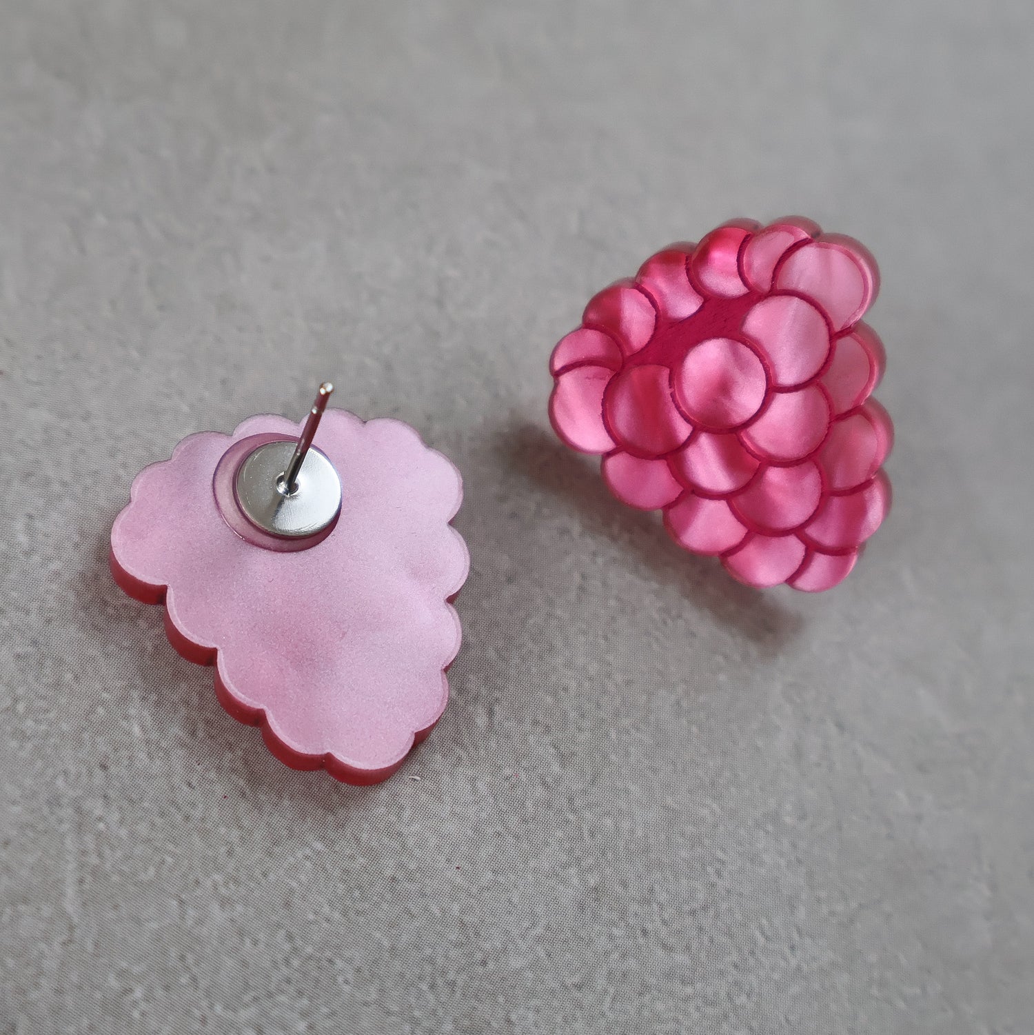 Pink raspberry acrylic earrings on a gray background. One earring is turned to show the stainless steel post on the back.