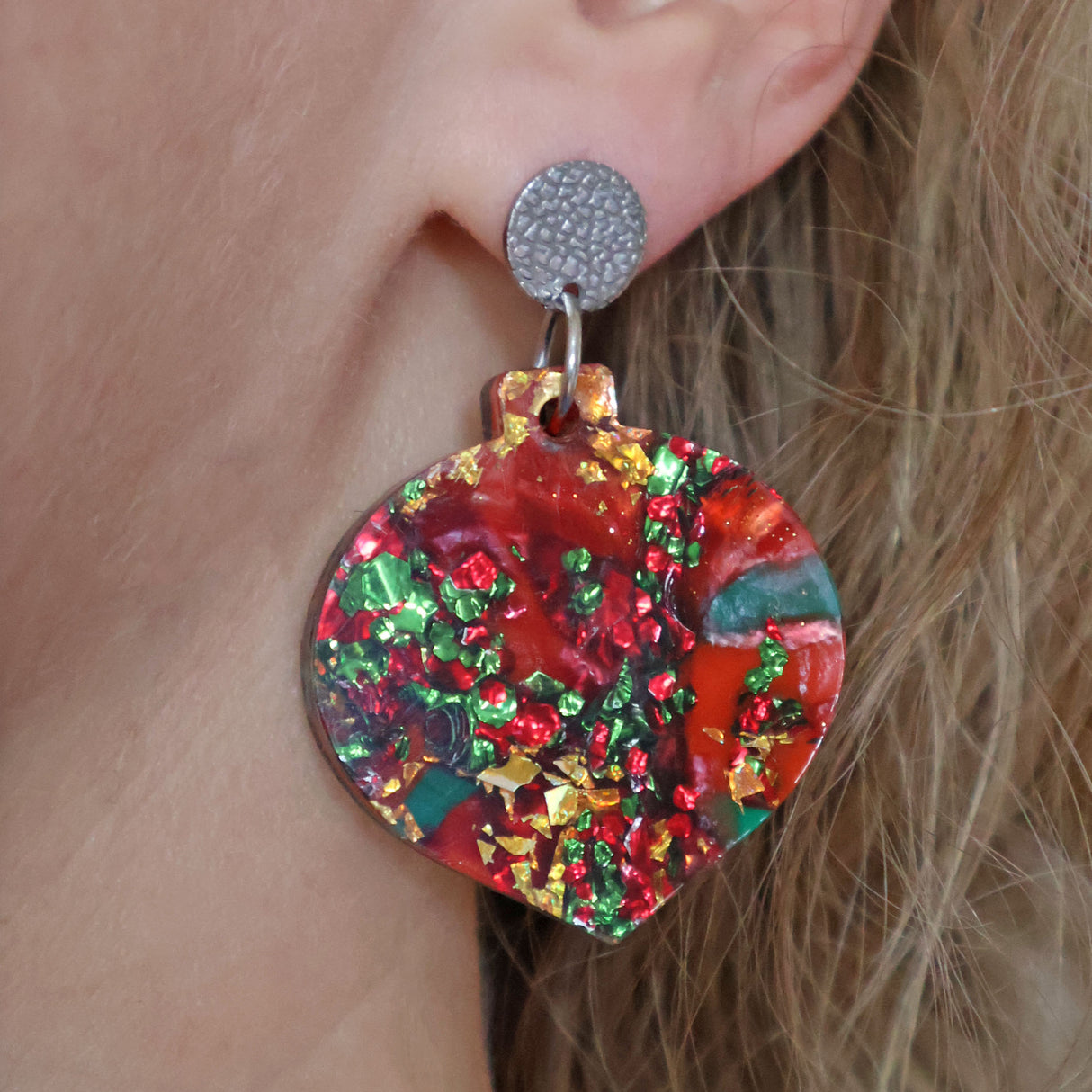 A pair of one of a kind recycled acrylic Christmas bauble earrings with stainless steel toppers, featuring a red, green and gold acrylic design being modelled.