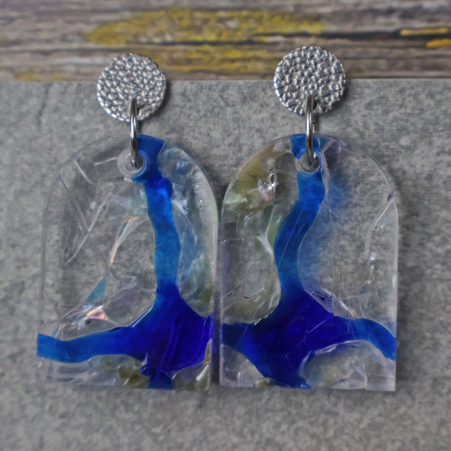 A pair of one of a kind arch shaped recycled acrylic earrings with blue, clear and pearlescent acrylics titled  'Aurora Shards' and stainless steel toppers. Pair 100-07