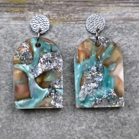 A pair of one of a kind arch shaped recycled acrylic earrings with silver, green and brown design titled 'Celestial Tide' and stainless steel toppers. Pair 102-01