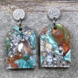 A pair of one of a kind arch shaped recycled acrylic earrings with silver, green and brown design titled 'Celestial Tide' and stainless steel toppers. Pair 102-06