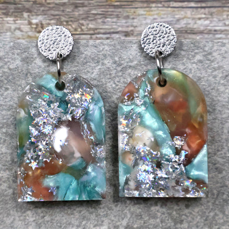 A pair of one of a kind arch shaped recycled acrylic earrings with silver, green and brown design titled 'Celestial Tide' and stainless steel toppers. Pair 102-06
