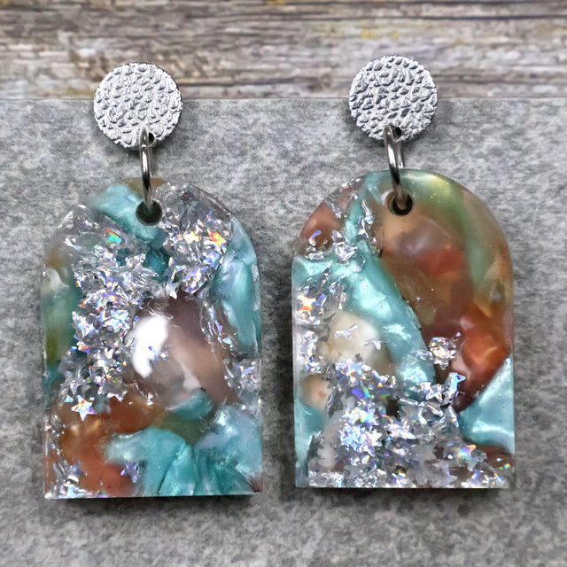 A pair of one of a kind arch shaped recycled acrylic earrings with silver, green and brown design titled 'Celestial Tide' and stainless steel toppers. Pair 102-06