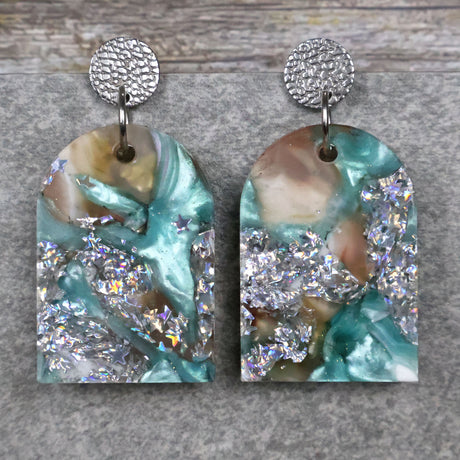 A pair of one of a kind arch shaped recycled acrylic earrings with silver, green and brown design titled 'Celestial Tide' and stainless steel toppers. Pair 102-07