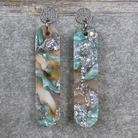 A pair of one of a kind long oval shaped recycled acrylic earrings with silver, green and brown design titled 'Celestial Tide' and stainless steel toppers. Pair 102-11