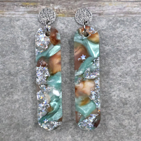 A pair of one of a kind long oval shaped recycled acrylic earrings with silver, green and brown design titled 'Celestial Tide' and stainless steel toppers. Pair 102-13