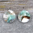 A pair of one of a kind round recycled acrylic earrings with stainless steel french hooks and silver, green and brown design titled 'Celestial Tide' Pair 106-17