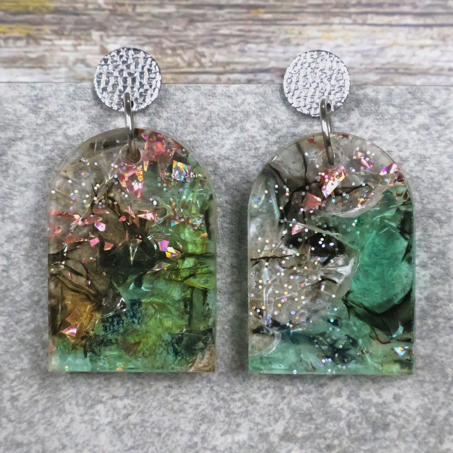 A pair of one of a kind arch shaped recycled acrylic earrings with green and pink design titled 'Enchanted Forest' and stainless steel toppers. Pair 103-02