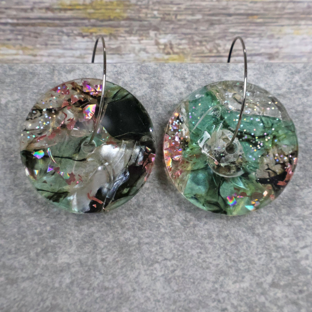 A pair of one of a kind disc shaped recycled acrylic earrings on stainless steel hoops with green and pink acrylics titled 'Enchanted Forest'. Pair 03-10