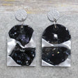 A pair of one of a kind arch shaped recycled acrylic earrings with black and white design titled 'Lunar Edge' and stainless steel toppers. Pair 104-01