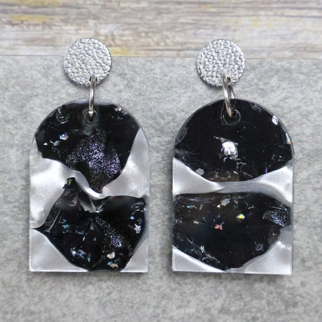 A pair of one of a kind arch shaped recycled acrylic earrings with black and white design titled 'Lunar Edge' and stainless steel toppers. Pair 104-01