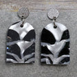 A pair of one of a kind arch shaped recycled acrylic earrings with black and white design titled 'Lunar Edge' and stainless steel toppers. Pair 104-04