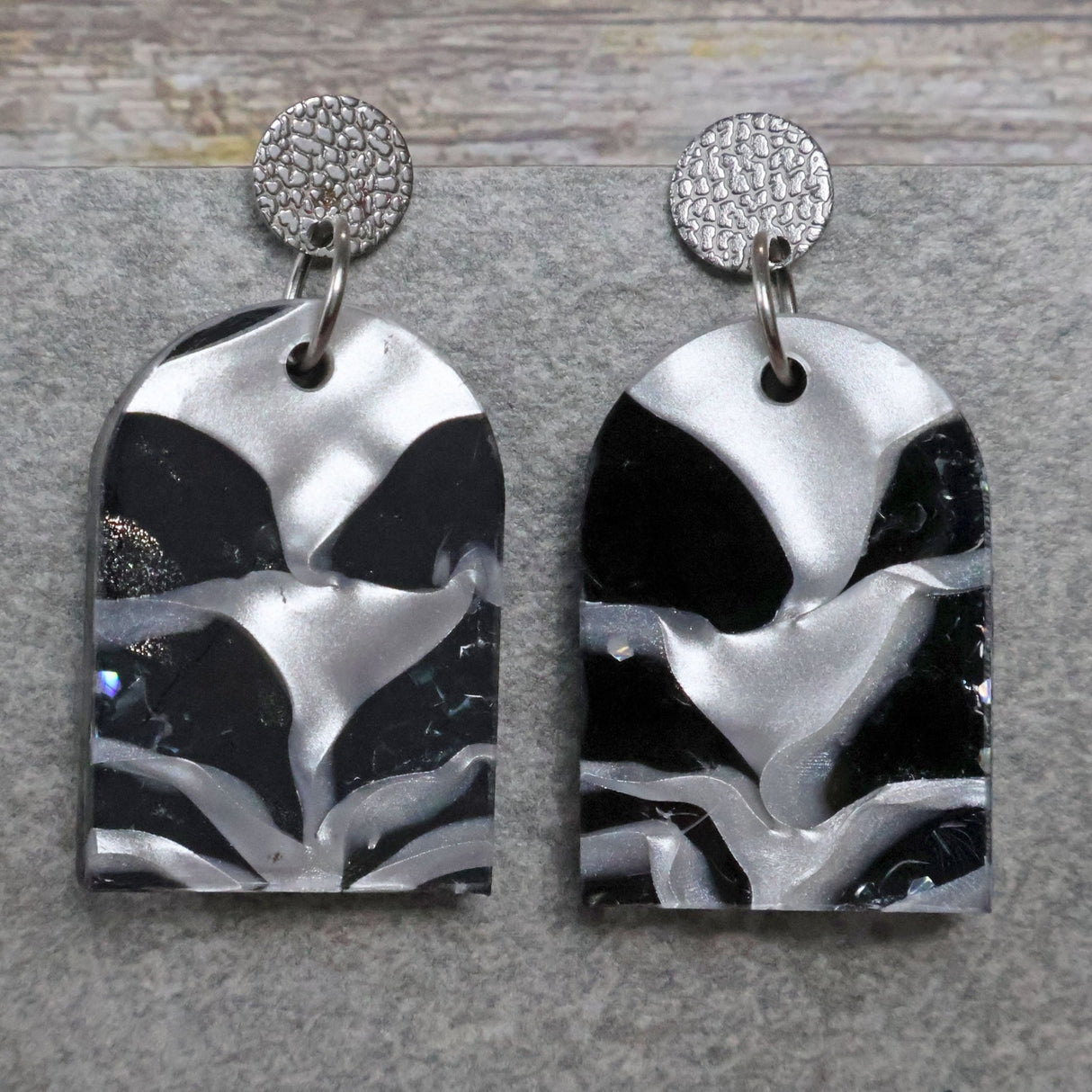 A pair of one of a kind arch shaped recycled acrylic earrings with black and white design titled 'Lunar Edge' and stainless steel toppers. Pair 104-04