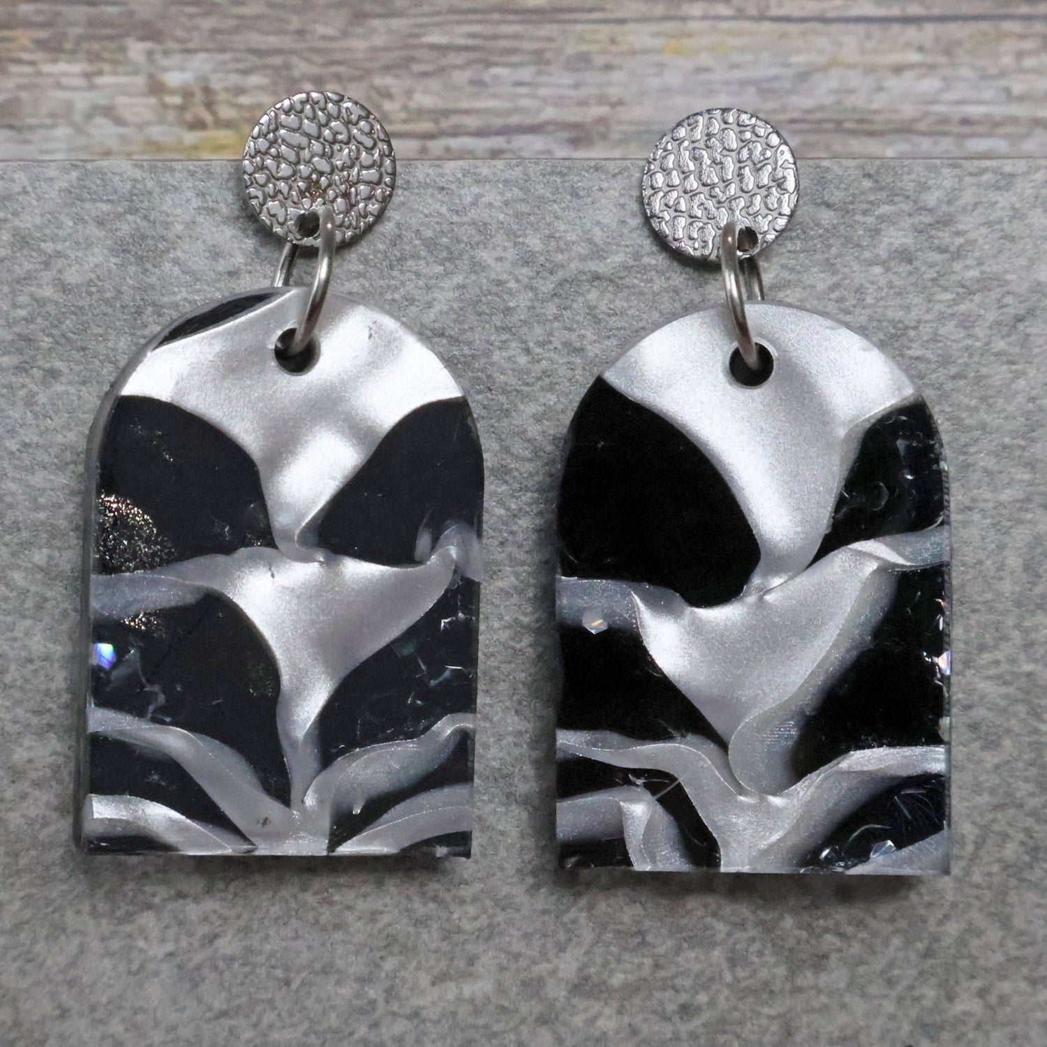 A pair of one of a kind arch shaped recycled acrylic earrings with black and white design titled 'Lunar Edge' and stainless steel toppers. Pair 104-04