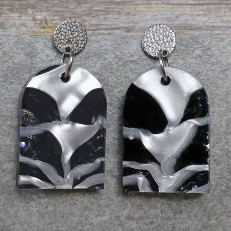 A pair of one of a kind arch shaped recycled acrylic earrings with black and white design titled 'Lunar Edge' and stainless steel toppers. Pair 104-04