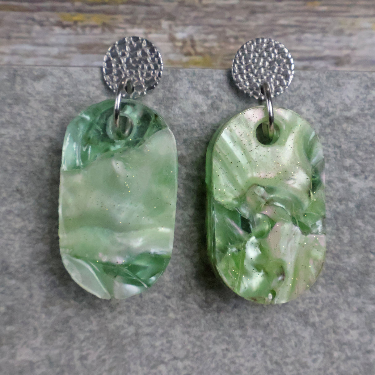 Pair of one of a kind small oval shaped recycled acrylic earrings featuring green acrylics and stainless steel toppers. Pair 105-06