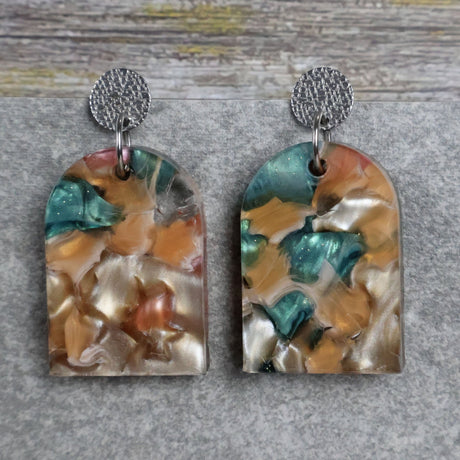 Pair of one of a kind arch shaped acrylic earrings with multicolored  design titled 'Sunset Reef' and stainless steel toppers on a gray background. Pair 106-04