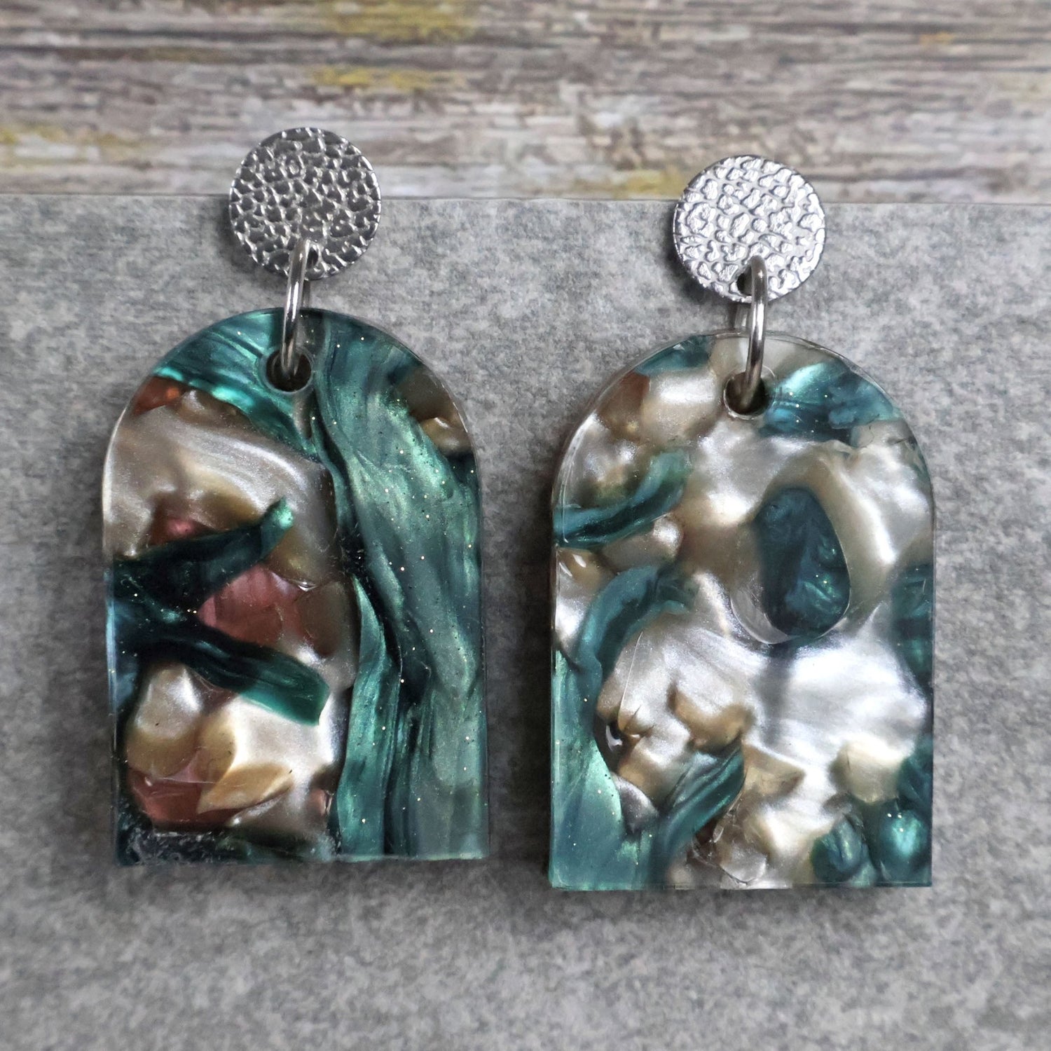 Pair of one of a kind arch shaped acrylic earrings with multicolored  design titled 'Sunset Reef' and stainless steel toppers on a gray background. Pair 106-05