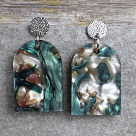 Pair of one of a kind arch shaped acrylic earrings with multicolored  design titled 'Sunset Reef' and stainless steel toppers on a gray background. Pair 106-05