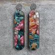 Pair of one of a kind long bar shaped acrylic earrings with multicolored  design titled 'Sunset Reef' and stainless steel toppers on a gray background. Pair 106-07