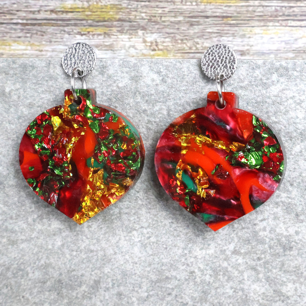 A pair of one of a kind recycled acrylic Christmas bauble earrings with stainless steel toppers, featuring a red, green and gold acrylic design. Pair 107-02