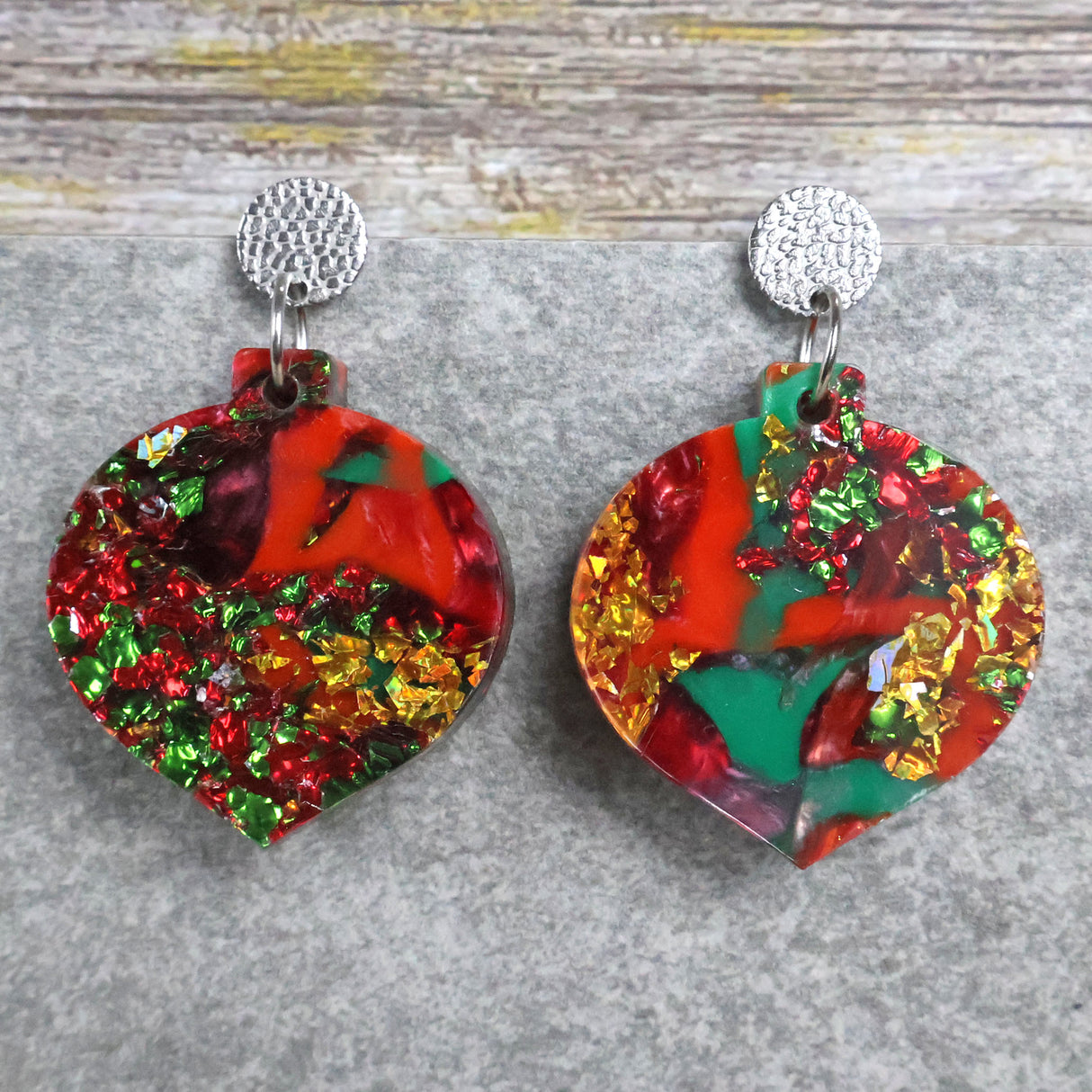 A pair of one of a kind recycled acrylic Christmas bauble earrings with stainless steel toppers, featuring a red, green and gold acrylic design. Pair 107-03