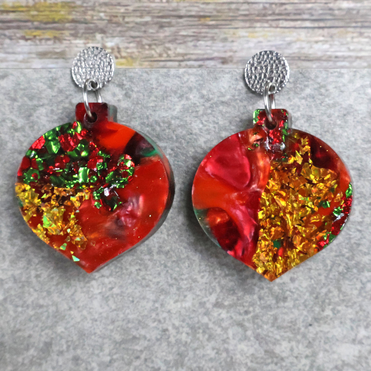 A pair of one of a kind recycled acrylic Christmas bauble earrings with stainless steel toppers, featuring a red, green and gold acrylic design. Pair 107-04