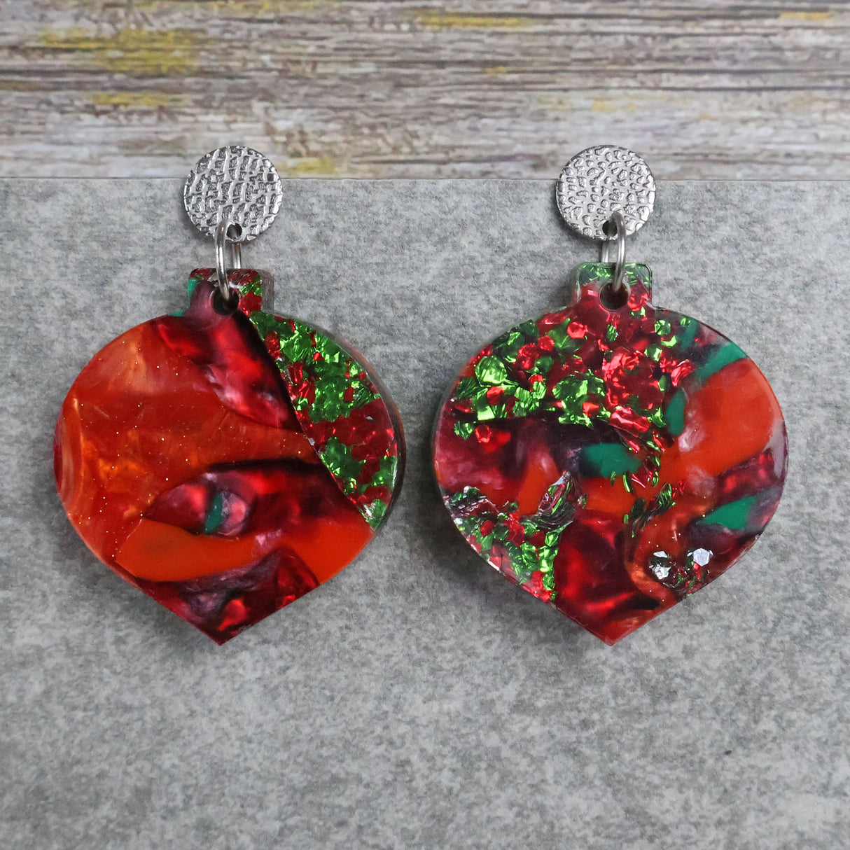 A pair of one of a kind recycled acrylic Christmas bauble earrings with stainless steel toppers, featuring a red, green and gold acrylic design. Pair 107-06