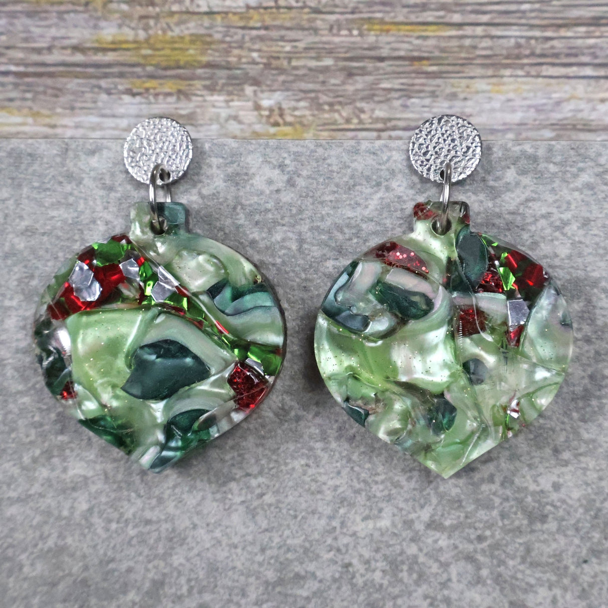 A pair of one of a kind recycled acrylic Christmas bauble earrings with stainless steel toppers, featuring a red and green acrylic design. Pair 109-02