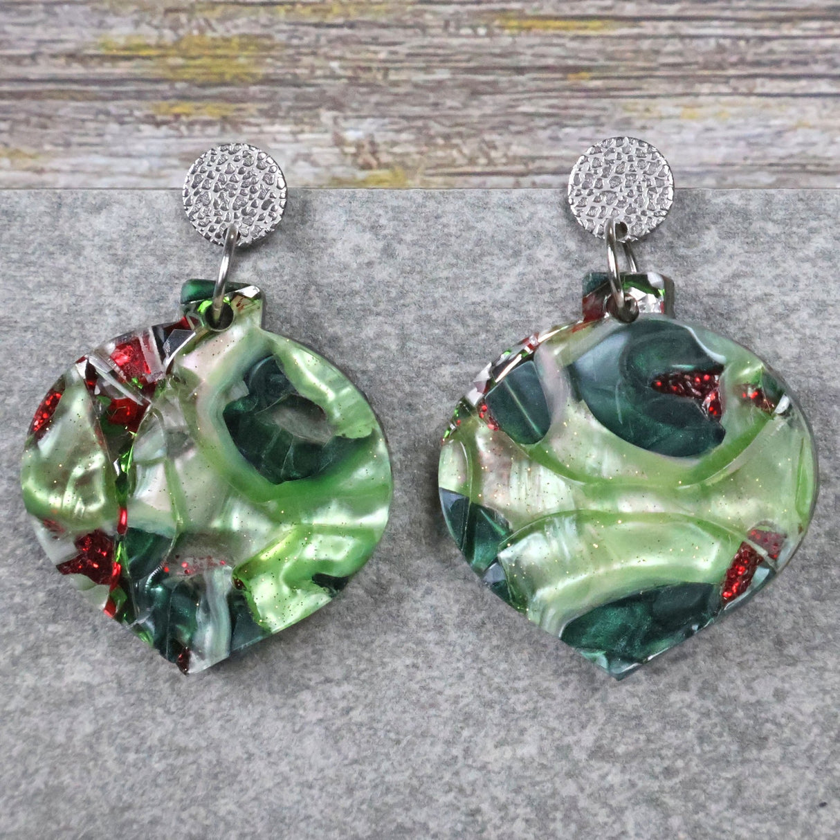 Pair of green and red bauble shaped earrings on a grey surface