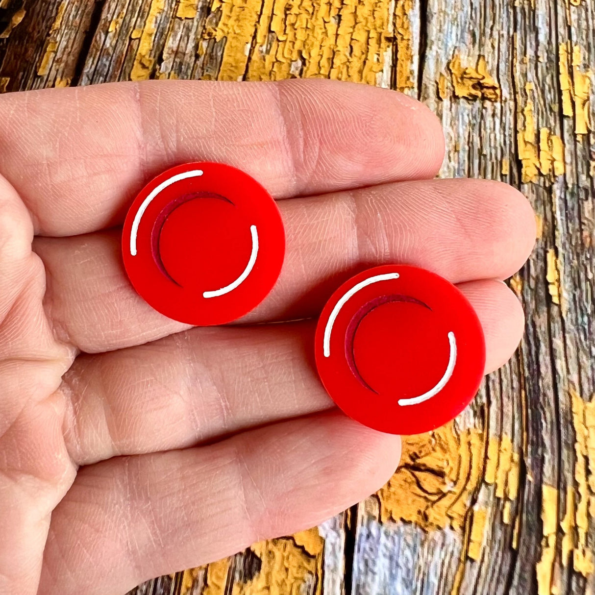 A pair of small round red blood cell studs, laser cut and handainted from red acrylic. Closeup view.