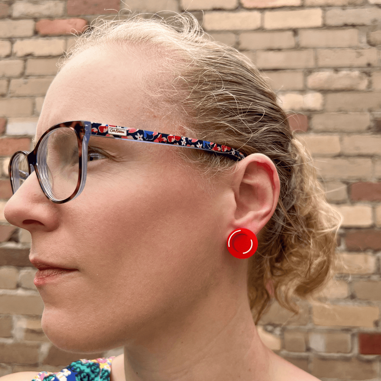 A red blood cell stud being modelled by the maker, a blonde woman with glasses. Studs are laser cut and handpainted from acrylic.