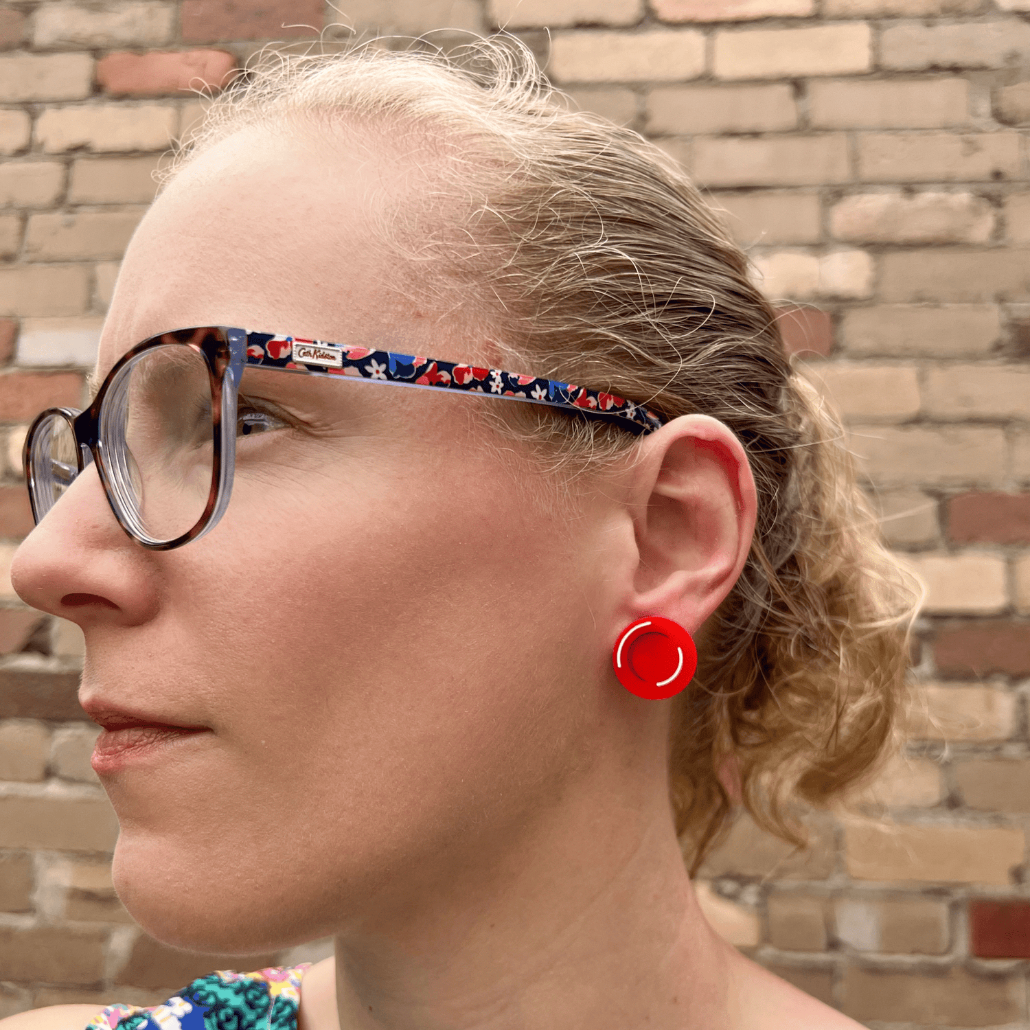 A red blood cell stud being modelled by the maker, a blonde woman with glasses. Studs are laser cut and handpainted from acrylic.