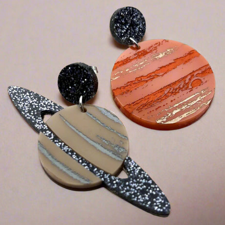A pair of asymmetrical earrings, of Jupiter and Saturn. Laser cut from acrylic with handpainted details.