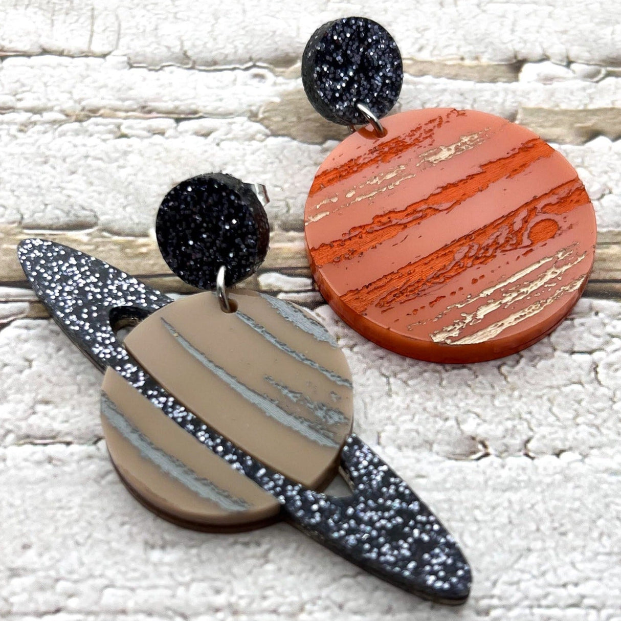 A pair of asymmetrical earrings, of Jupiter and Saturn. Laser cut from acrylic with handpainted details.