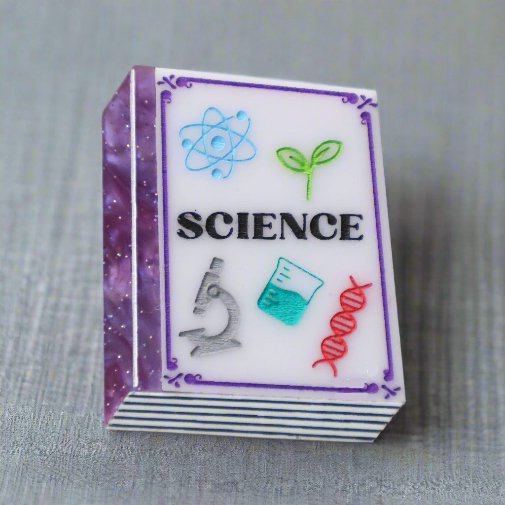 Small purple toned book brooch with 'SCIENCE' and related icons